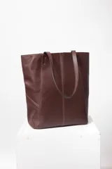 Bolso tote de cuero marrón con costuras a la vista y doble bolsillo interior, uno con cierre. Cierra con broche imán.