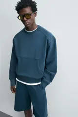 Sudadera azul petróleo de corte relajado, cuello redondo, manga larga, bolsillo tipo canguro y terminaciones en rib.