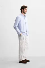 Camisa celeste con rayas verticales blancas, de corte regular, cuello solapa, manga larga con puños abotonados y cierre frontal con botones.