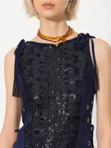 Top corto sin mangas de gamuza azul marino con tela bordada con lentejuelas en el frente. Breteles que se anudan sobre los hombros y ojalillos metálicos en los laterales con tiento de gamuza para ajustar la cintura. Cierre metálico en la espalda.