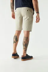 Bermuda color beige, de corte chino clásico, con bolsillos laterales y traseros, cierre con botón y cremallera, presillas para cinturón y logo bordado. Confeccionada en algodón y spandex.