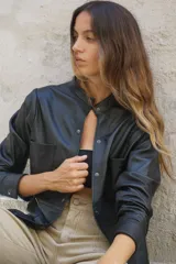 Camisa negra de cuero ovino con cuello mao, cierre frontal con botones a presión, dos bolsillos de parche en el pecho y tachas doradas en cuello, bolsillos y puños.