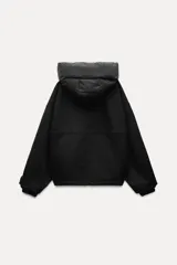 Chaqueta negra de cuello redondo confeccionada en hilatura con 50% lana. Tiene capucha extraíble, manga larga con puño interior, bolsillos delanteros y bajo ajustable con cordón elástico. Cierre frontal con cremallera metálica.