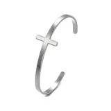 Pulsera rígida abierta de acero quirúrgico color plateado, con un dije de cruz en el centro.