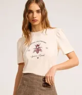 Blusa slim de algodón color crema, con cuello redondo y mangas cortas abullonadas. Presenta un estampado con lettering en inglés y una ilustración de una abeja.