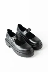 Mocasín negro de cuero con hebilla plateada y suela track.
