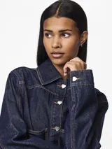 Chaqueta de denim azul oscuro con cuello camisero, cierre frontal con botones en forma de corazón, bolsillos delanteros y costuras en contraste color ocre.