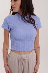 Blusa de punto color lavanda, de corte corto y mangas cortas con acabados ondulados.