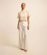 Blusa de mangas cortas confeccionada en chiffon color crema, con cuello alto, cavas raglán, cierre por gota y textura rayada.