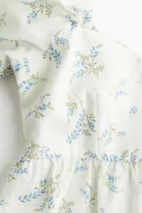 Vestido corto blanco con estampado de flores azules, escote corazón, mangas cortas abullonadas con elástico en hombros y puños, espalda fruncida, corte ajustado en el busto y falda con vuelo y costura fruncida en el bajo.
