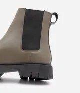 Bota Chelsea color verde oliva, confeccionada en cuero sintético, con laterales elásticos negros y suela track negra.