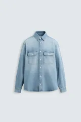 Camisa celeste de denim de algodón, corte relaxed fit, con cuello solapa, manga larga con puños abotonados, dos bolsillos de parche con solapa en el pecho, efecto lavado y cierre frontal abotonado.