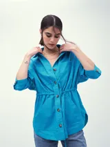 Chaqueta color beige con cuello camisero, cierre frontal con botones, cintura ajustable con cordón y cuatro bolsillos frontales.