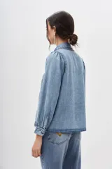 Camisa de denim celeste con bordados geométricos en el frente, corte recto, cuello camisero, manga larga con frunces en los hombros y puños abotonados.