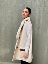 Chaleco largo color beige tejido en lana merino, con cuello alto y cierre frontal con botones de madera.