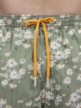 Short de baño verde con estampado de margaritas blancas y cordón ajustable naranja.