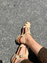 Sandalias nude de cuero con diseño calado y tira con hebilla al tobillo.