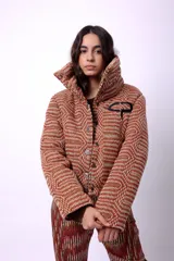 Campera corta con estampado abstracto en tonos marrones y beige, cuello alto, cierre frontal con botones a presión, bolsillos delanteros y bordado negro con las iniciales CP. Forro interior y relleno liviano de guata.