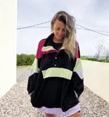 Buzo negro con bloques de color fucsia, verde y lila, con cuello alto con cierre y botones a presión.