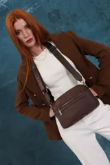 Bandolera color rosa viejo con detalles en cuero marrón claro, múltiples cremalleras metálicas y herrajes plateados. Incluye correa ancha ajustable con el logo de la marca.