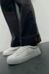 Zapatilla blanca con logo bordado, diseño clásico y suela plana.