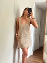 Vestido corto de tejido de punto color beige/dorado, con escote redondo y tirantes anchos. Presenta un tejido acanalado verticalmente con hilos de lurex que le dan brillo.