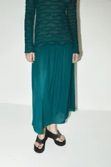 Vestido midi color verde esmeralda con textura plisada en la parte superior y falda lisa. Tiene cuello redondo y mangas largas.