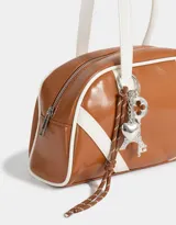 Cartera bowling marrón con detalles en blanco, doble asa corta de hombro y charms decorativos de metal plateado con forma de Torre Eiffel, corazón y llave.