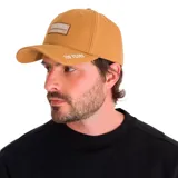 Gorra color ocre con parche frontal con el logo de Caterpillar y la leyenda "A Tractor Co. Since 1925". Tiene visera curva y correa ajustable en la parte posterior.