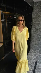 Vestido largo color amarillo pálido, con escote en V, mangas cortas abullonadas con detalle de calado y ruedo con volantes y calado.