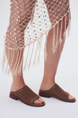 Sandalias bajas de cuero color beige con detalle de tachas metálicas en la tira delantera.