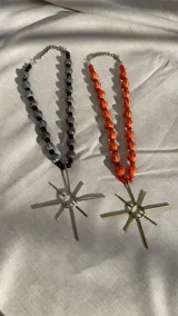 Collar con cadena de eslabones plateados y cuentas de cerámica y vidrio en color negro y gris, con dije de sol plateado. También disponible con cuentas de cerámica y vidrio en color naranja y dije de sol dorado.