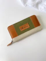 Billetera grande con cierre metálico, confeccionada en cuero con diseño de bloques de color: verde oliva texturizado, marrón claro liso y blanco/crema texturizado. Posee un monedero interno y un tirador de cuero marrón claro.