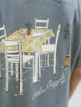 Remera azul con estampado de una mesa con sillas, una planta y luces colgantes.