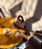 Cartera tipo tote de cuero color beige, con doble asa corta marrón y cierre superior con cremallera. Tiene un bolsillo frontal con cremallera y forro interior de tela con un bolsillo.