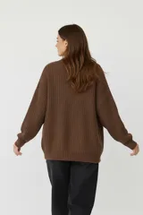 Cardigan de punto acrílico color crema, con cuello en V, manga larga y botones frontales. Presenta un tejido acanalado grueso y un calce holgado.