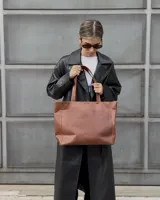 Cartera tipo tote de cuero graneado color negro, con textura uniforme y suave al tacto. Tiene manijas de 55 cm, bolsillo frontal con broche imantado, bolsillo trasero con cierre metálico, cierre principal metálico, forro interior y tres bolsillos internos (uno con cierre, uno plaqué y uno tipo sobre con solapa y botón).