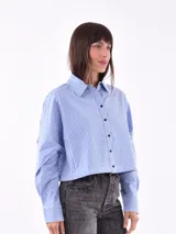 Camisa corta a la cintura, a rayas verticales azules y blancas, con cuello clásico y cierre frontal con botones negros.