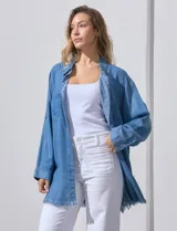 Camisa de jean celeste, marca Hester & Orchand, de corte oversize con cuello con solapa, escote en V y abertura central con botones. Delantera con bolsillos aplicados, mangas largas regulables con presilla y botón, y ruedo desflecado.