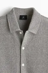 Camisa gris de manga corta en tejido piqué con cuello inglés, tapeta lisa, canesú en la espalda y bajo recto con aberturas laterales.