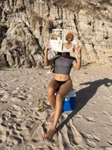 Top de bikini o crop top negro con estampado de lunares blancos, escote bardot (hombros descubiertos) y mangas cortas.