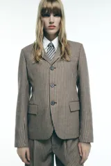 Blazer de cuello solapa y manga larga con estampado de cuadros en tonos marrón y blanco. Tiene bolsillos con solapa en el delantero, abertura en la espalda y cierre frontal con botones.