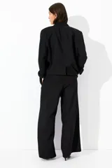 Pantalón negro de corte ancho, tiro alto, con bolsillos al bies y cierre oculto.