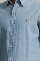 Camisa de hombre marca Polo Ralph Lauren, de manga larga, color celeste claro, confeccionada en tela chambray de algodón. Tiene cuello abotonado y logo bordado en el pecho.