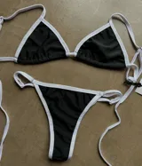 Conjunto de bikini negro con ribete blanco en contraste, compuesto por corpiño triangular con tirantes finos y bombacha tipo tanga con tirantes finos.