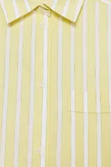 Camisa tipo pijamera a rayas amarillas y blancas, confeccionada en hilatura con algodón y lino. Tiene cuello solapa, manga larga con puños y cierre frontal con botones.