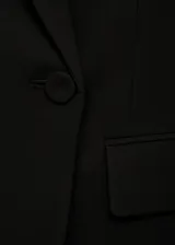 Blazer negro de corte recto, con cuello de pico cruzado y cierre de un solo botón. Presenta solapas con muesca, bolsillo de ribete en el pecho y dos bolsillos de solapa laterales.