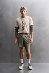 Shorts de entrenamiento color verde oliva, confeccionado en tejido técnico ligero y elástico con perforaciones. Tiene forro interior, cintura elástica ajustable con cordón, bolsillos laterales, bolsillo trasero con cierre de cremallera, bajo con aberturas laterales y logo estampado en la pierna.