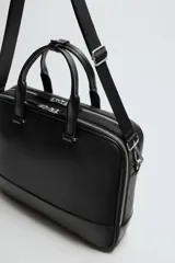 Maletín negro con acabado texturizado, compartimento principal con cierre de cremallera, bolsillo interior con cremallera, bolsillo frontal con cremallera, bolsillo trasero para dispositivos electrónicos de hasta 13 pulgadas y bolsillo trasero con cremallera. Tiene dos asas de mano y un asa de hombro ajustable y extraíble.