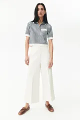 Pantalón palazzo color blanco hueso de tiro alto con elástico oculto en la cintura, cierre lateral oculto y pinzas que realzan la figura. Modelo de corte holgado con bolsillos al bies, bolsillos decorativos atrás y piernas tres cuartos con raya adelante y atrás.